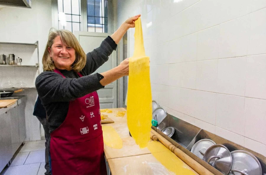 A pasta maker showing the perfect transparency of a hand-rolled "sfoglia" dough sheet in a professional kitchen.