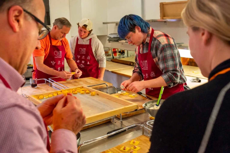 A group of students learning how to fold handmade tortelloni pasta during an authentic cooking class in Bologna, Italy.