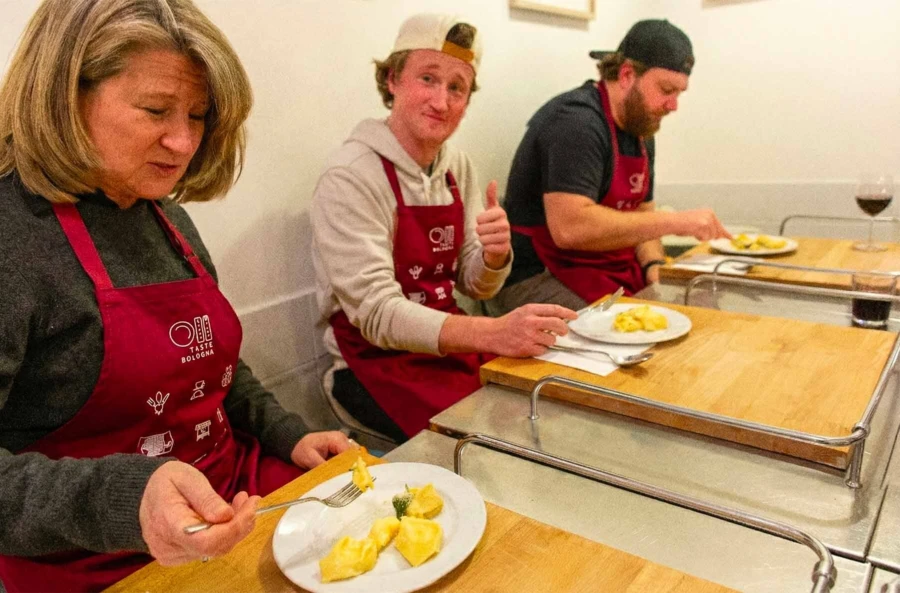 Happy travelers enjoying a meal of self-made fresh pasta and wine after a cooking lesson in Bologna.