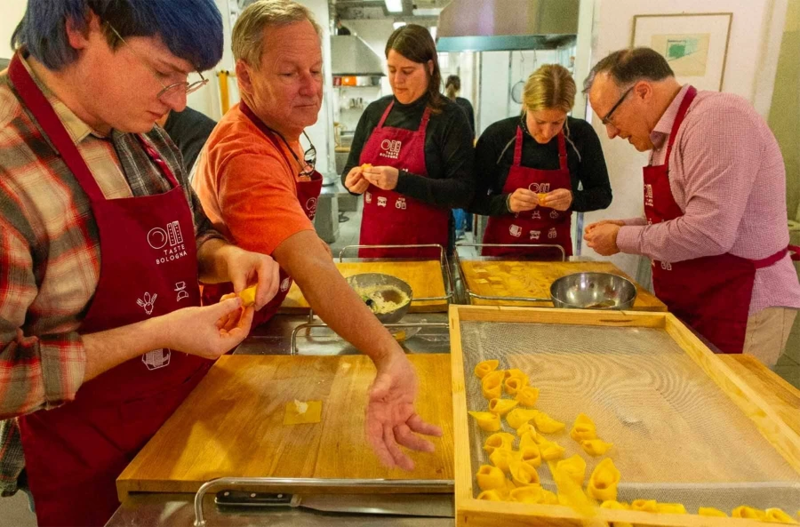 Close-up of participants placing ricotta filling on fresh pasta squares to make traditional tortelloni in a Bologna workshop.