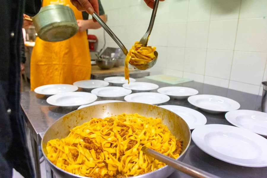Chef plating fresh handmade Tagliatelle al Ragù with authentic Bolognese meat sauce during a cooking class in Bologna.